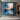 Abstract oil painting of sunset over water with orange and blue color gradients, textured brushstrokes, and dark mountain silhouettes on the horizon.