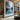 Abstract oil painting of sunset over water with orange and blue color gradients, textured brushstrokes, and dark mountain silhouettes on the horizon.
