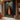 Abstract oil painting of two elongated black silhouettes standing in a vibrant orange light pathway, dark charcoal background enhancing dramatic contrast.  